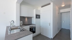 A modern kitchen with white cabinets, a stainless steel sink, a kettle, and a microwave. - Stylish flat with sea view (Koksijde)