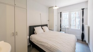 A bedroom with a bed, a wardrobe, a window with curtains, and a radiator. - Stylish flat with sea view (Koksijde)