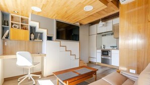 Un interior moderno con techo de madera, una zona de cocina, un espacio de estar con sofá y un escritorio con silla.