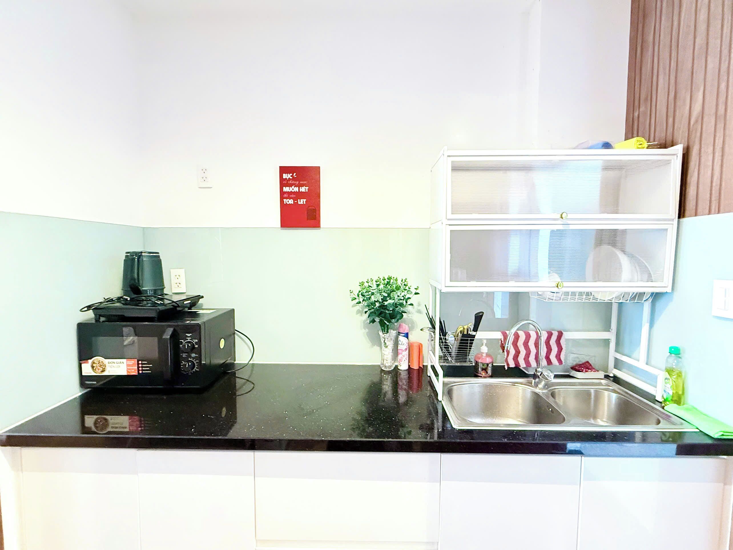 Cocina compacta con microondas, un lavamanos pequeño y una repisa con vajilla.