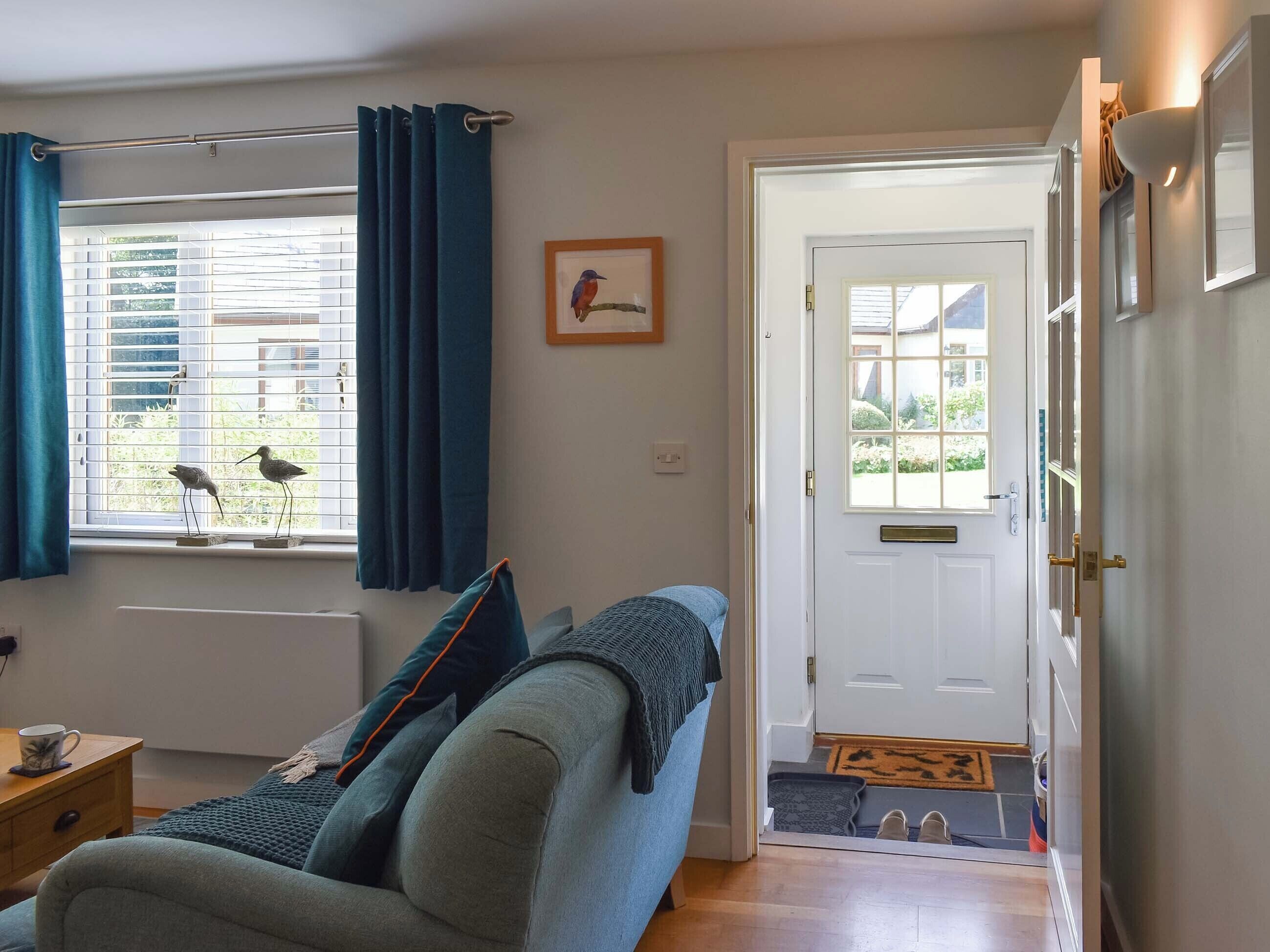 A cozy living room with a sofa, a window with curtains, a door, and a small table with a cup.