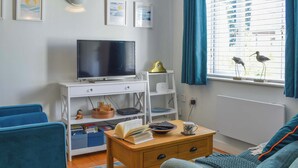Ett modernt vardagsrum med en platt-TV, ett soffbord i trä, en blå soffa och ett fönster med blå gardiner.