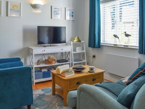 Un saló modern amb un televisor de pantalla plana, una taula baixa de fusta, un sofà blau i una finestra amb cortines blaves.