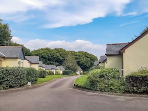 Une rue résidentielle bordée de maisons des deux côtés, un ciel dégagé et un panneau indiquant une limitation de vitesse à 5.