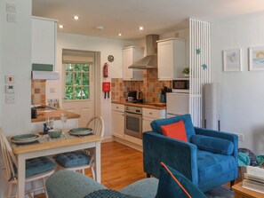 Een kleine keuken met een eethoek, een blauwe fauteuil en een tafeltje met een boek.