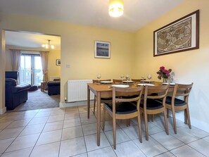 Uma área de refeições com uma mesa de madeira posta para quatro pessoas, um sofá, um radiador e um quadro na parede.