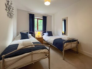 A room with two metal bunk beds, a window with curtains, a bedside table with a lamp, and a mirror on the wall. - A peaceful getaway on the outskirts of Whitby. (Whitby)