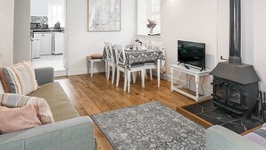 Ein Wohnzimmer mit Sofa, einem Esstisch mit Stühlen, einem Fernseher, einem Kamin und einer Küche im Hintergrund.