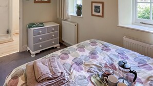 Ein Schlafzimmer mit Bett, Kommode, Heizkörper, Fenster und gerahmten Bildern an der Wand.