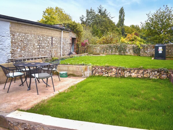 A patio with a table and chairs, a stone wall, a grassy yard, and a wooden fence.