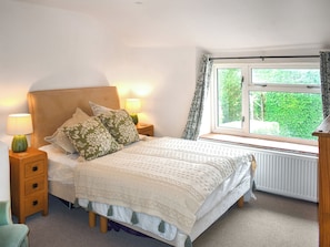 Une chambre à coucher avec un lit, des tables de chevet, une fenêtre avec des rideaux et une vue sur la verdure à l’extérieur.