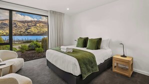 Un dormitorio con cama, mesita de noche, silla y vista a un lago y montañas.