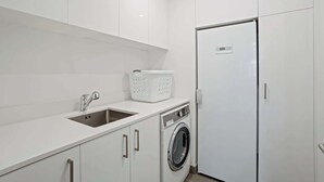 Un moderno cuarto de lavado con lavadora, un lavamanos y un armario blanco.