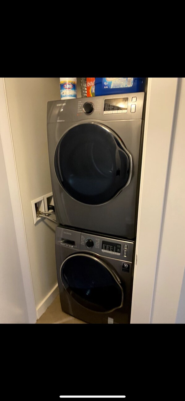 Un appareil combiné lave-linge et sèche-linge à chargement frontal, doté de panneaux de commande et d’un câble d’alimentation.
