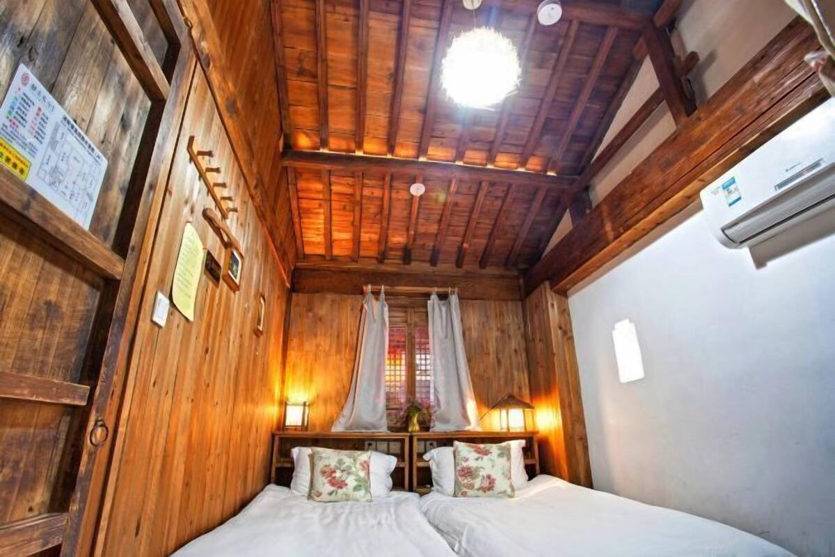 A wooden room with a bed, a window with curtains, a wall-mounted air conditioner, and a ceiling light fixture.