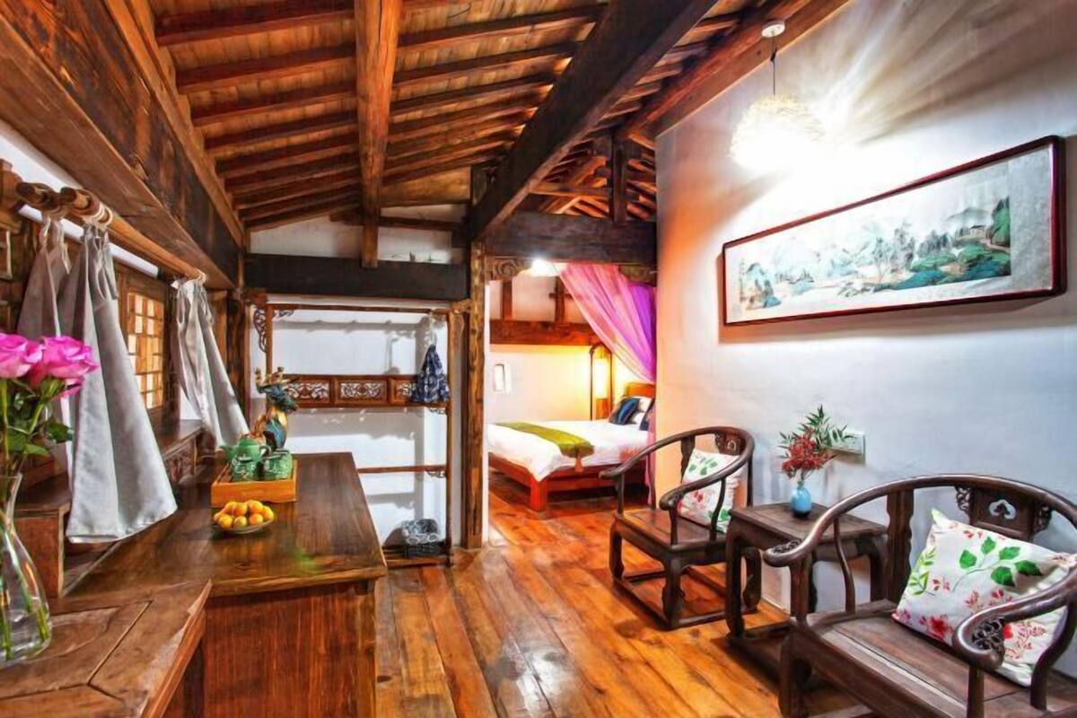 A traditional wooden interior with a bed, chairs, a table, and a painting on the wall.