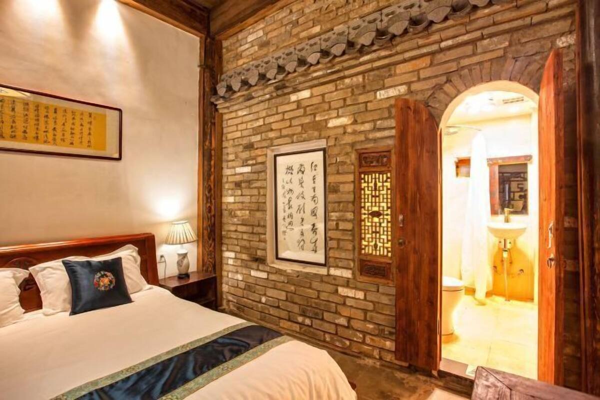 A traditional room with a brick wall, a wooden door, a bed with pillows, and a framed calligraphy piece.