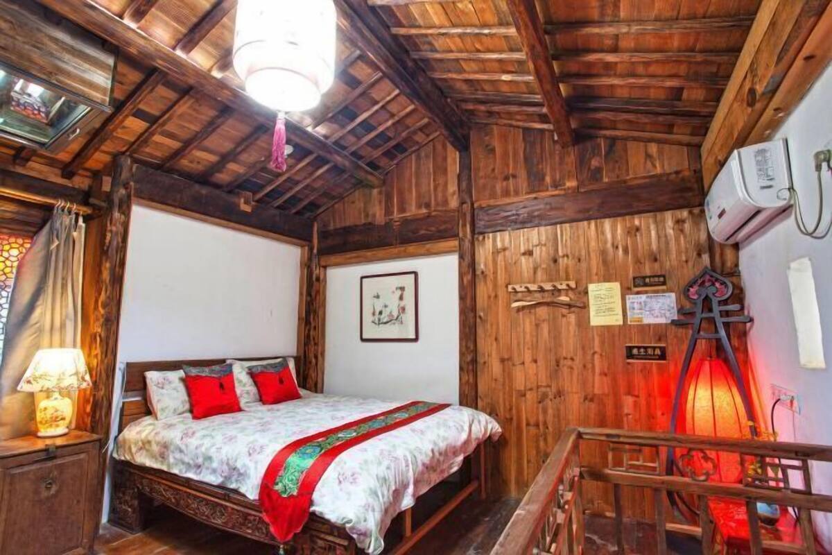 A wooden room with a bed, a nightstand, a wall-mounted air conditioner, and a lantern.