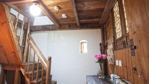 Μια ξύλινη σκάλα οδηγεί σε ένα δωμάτιο με ξύλινη πόρτα, ένα μικρό παράθυρο και ένα βάζο με λουλούδια πάνω σε ένα τραπέζι.