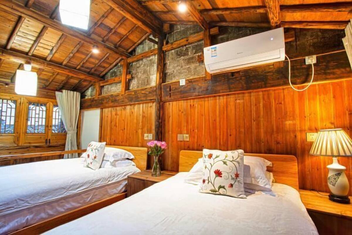 A wooden room with two beds, a window, and an air conditioning unit.