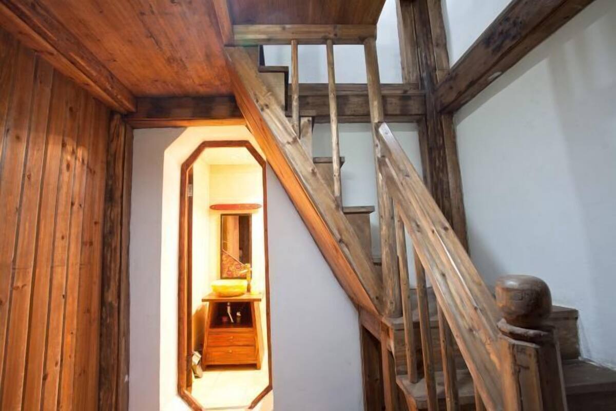 A wooden staircase with a handrail and a wooden door leading to a room with a window and a sink.