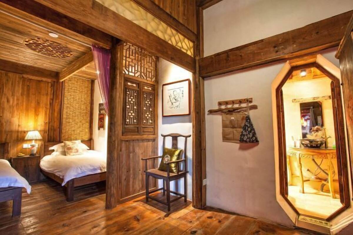 A wooden room with a bed, a chair, a wall with a geometric pattern, and a door leading to another room.