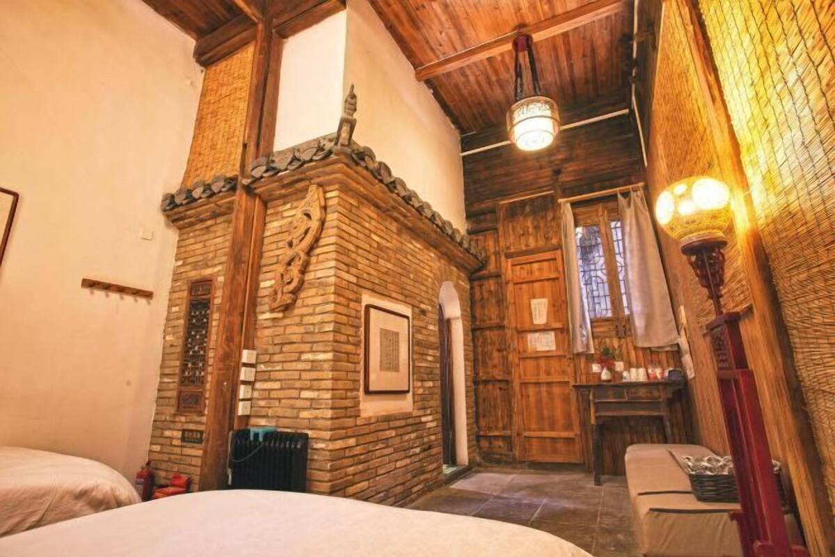 A rustic room with a brick fireplace, wooden beams, and a bed.