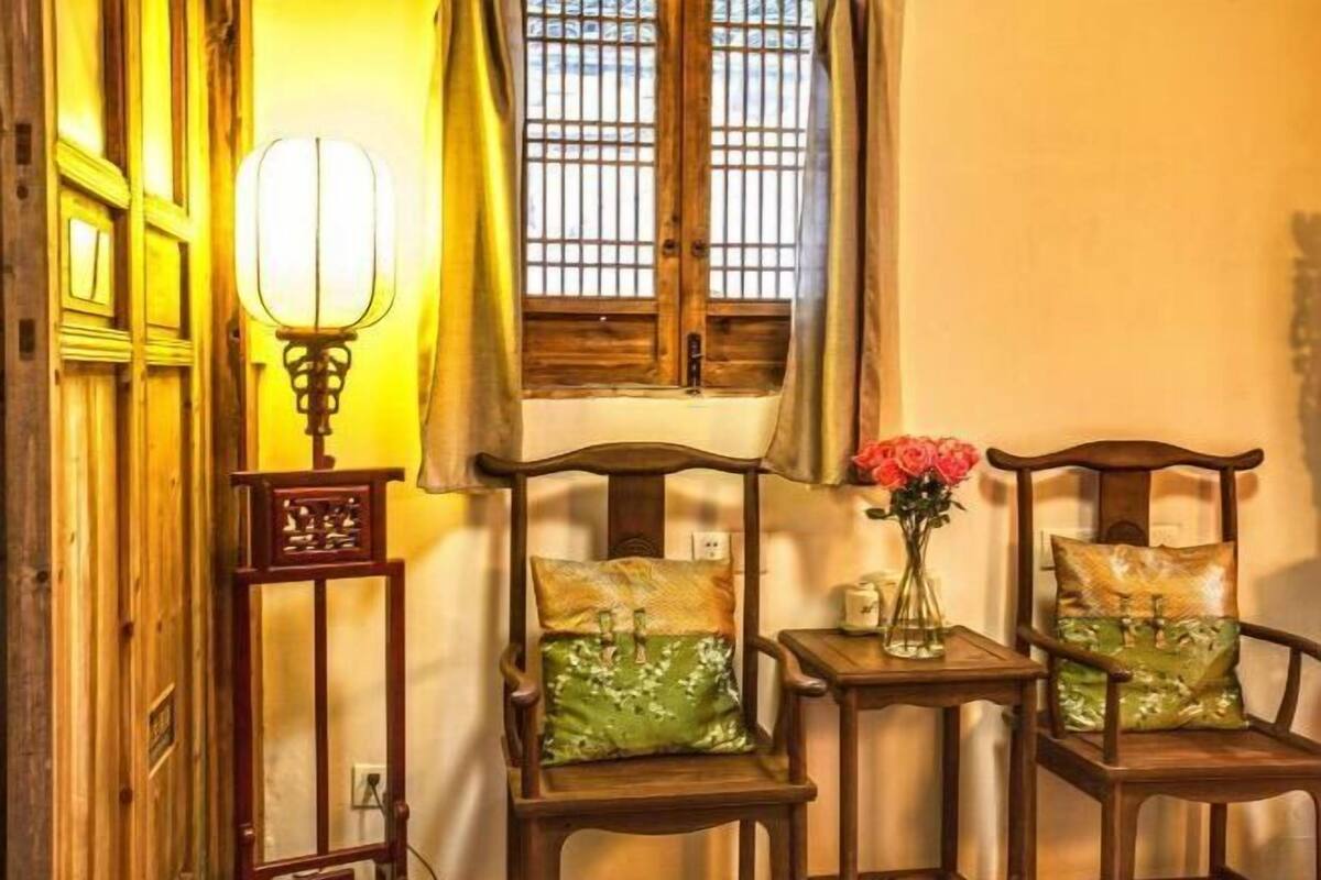 A traditional room with wooden furniture, a window with bars, a wall-mounted lamp, and a vase with flowers.
