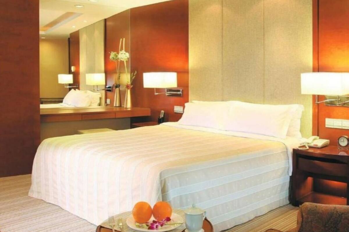 A hotel room with a large bed, bedside lamps, a nightstand, a mirror, and a small table with a plate of fruit and a cup.