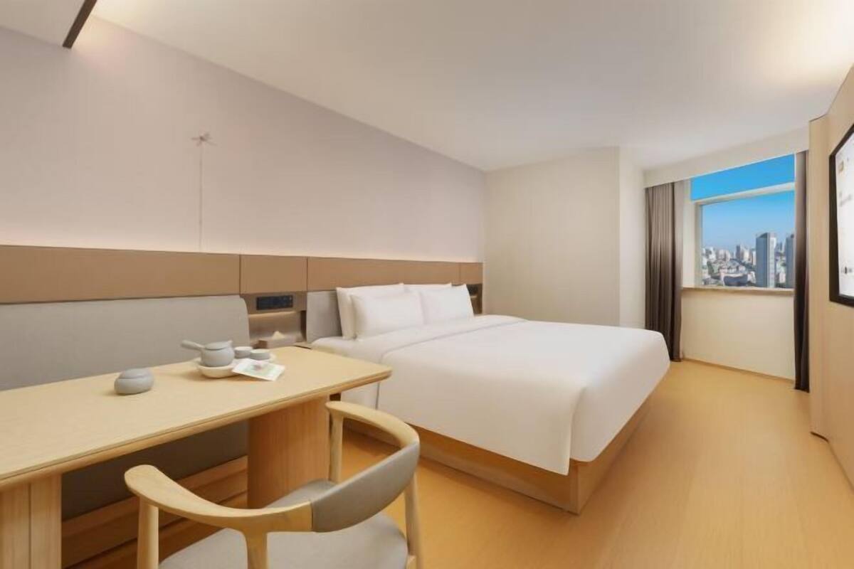 A hotel room with a bed, a desk, a chair, and a city view.