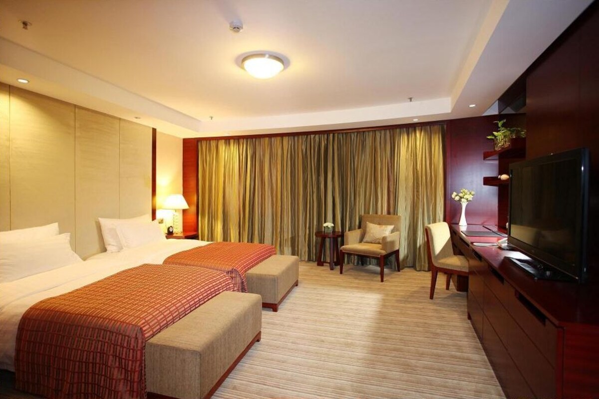 A hotel room with two beds, a TV, a desk, and a chair.
