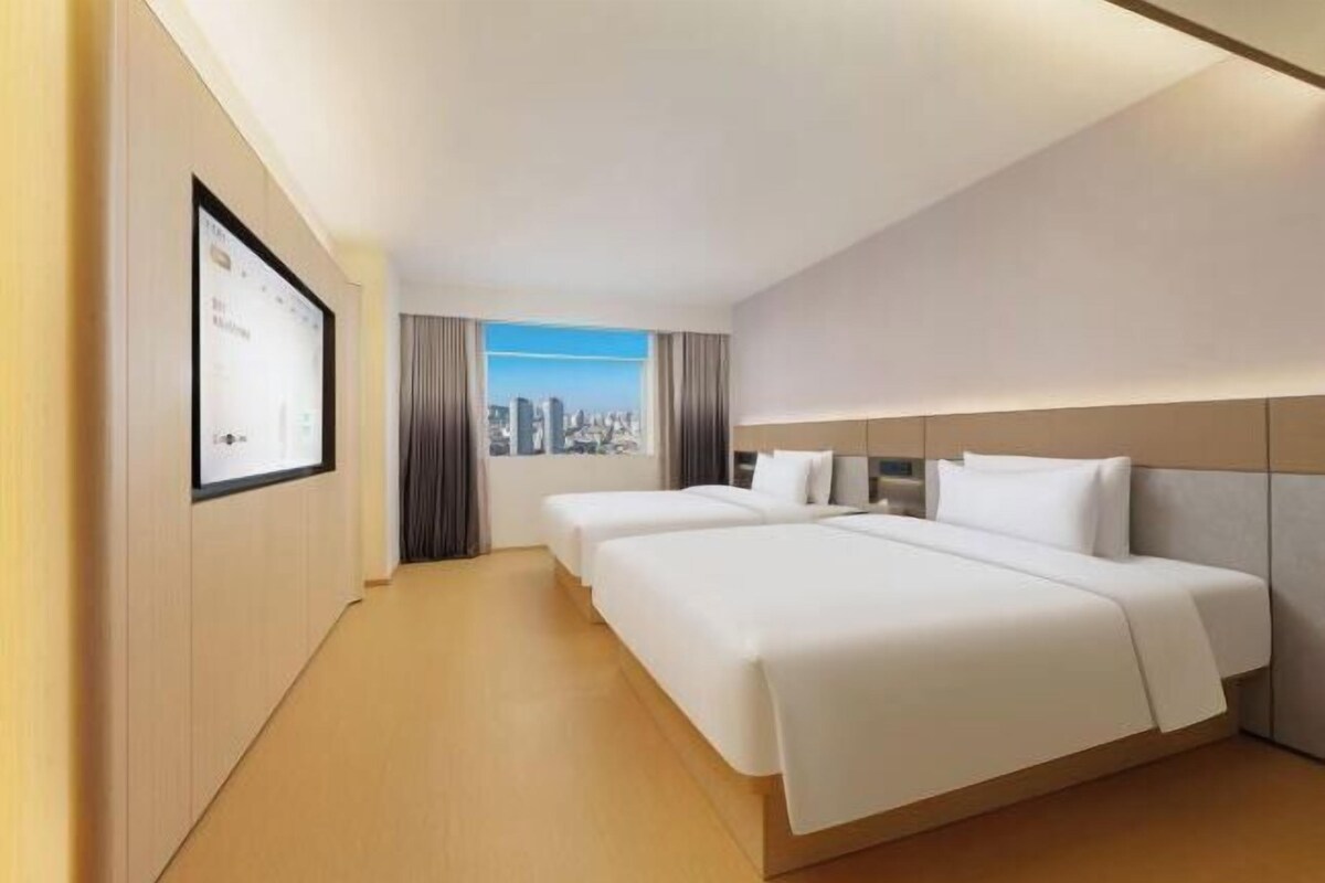 A hotel room with two beds, a city view, and a framed picture on the wall.