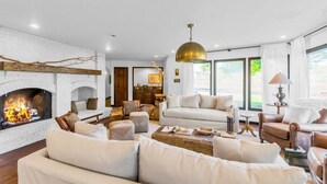 Una sala de estar con chimenea, sofás blancos, una mesa de centro y una lámpara colgante de latón.