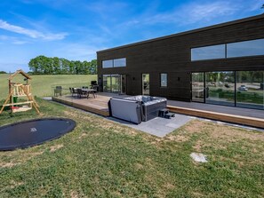 Una casa moderna con terraza, jacuzzi y una casita de juegos de madera.
