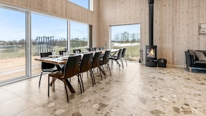 A spacious room with a large dining table, chairs, a fireplace, and large windows offering a view of the outdoors. - "Gillis" - 1km from the sea by Interhome (Glesborg)