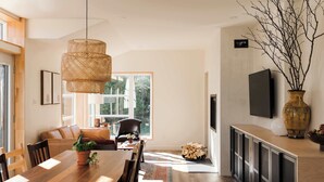 Un espace de repas moderne avec une table en bois, des chaises et un luminaire suspendu en rotin. Une grande fenêtre offre une lumière naturelle et une vue sur l’extérieur.