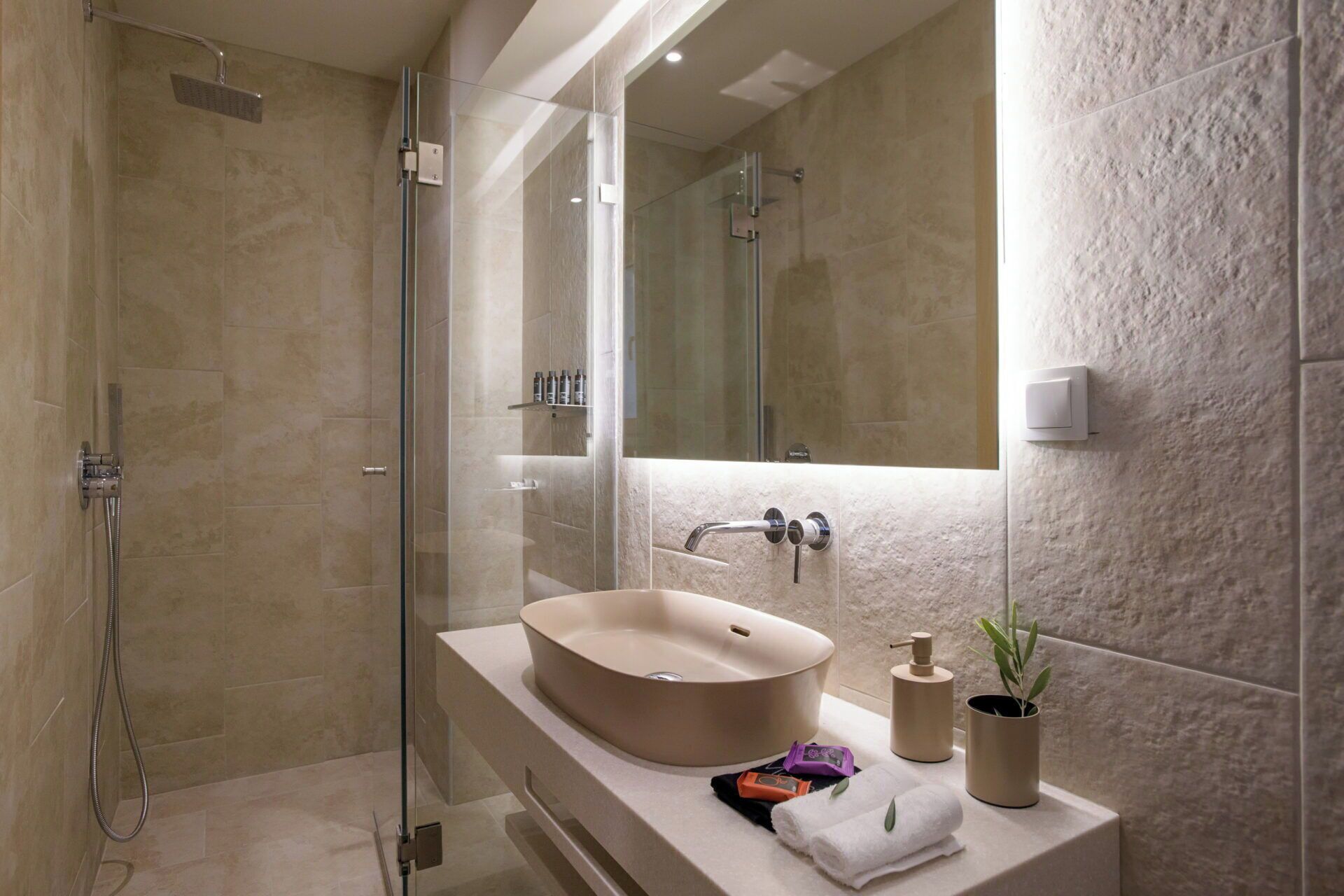 Un bagno moderno con doccia vetrata, un lavandino color beige e uno specchio grande.