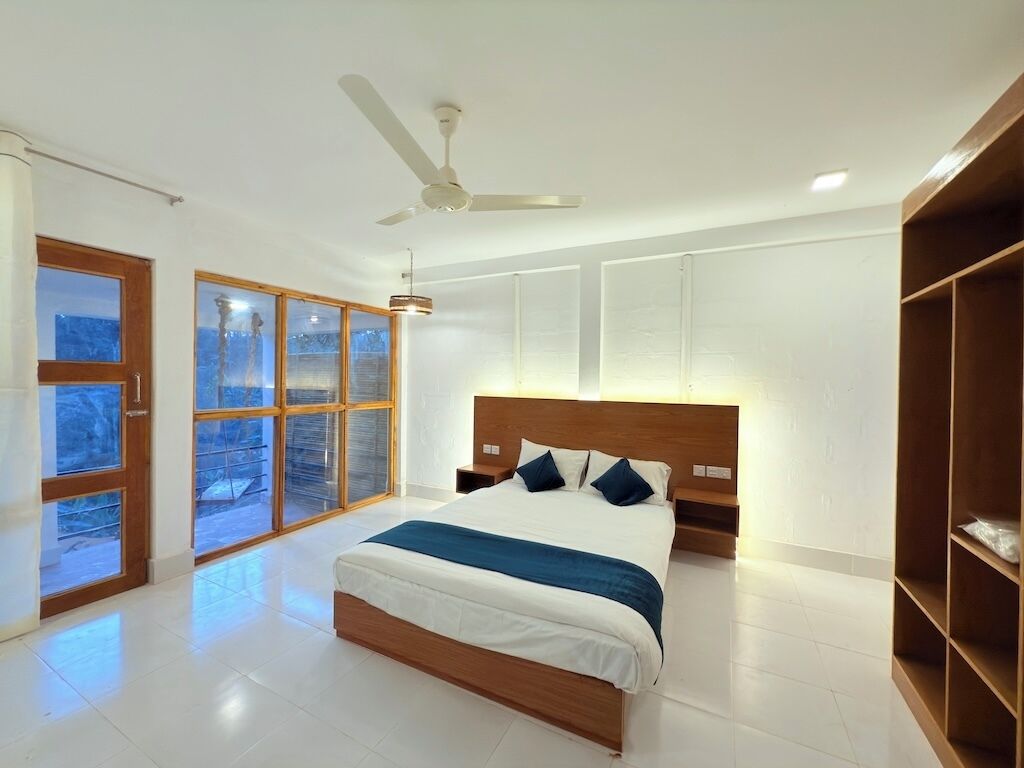 A modern bedroom with a large bed, a ceiling fan, and a view through the windows.