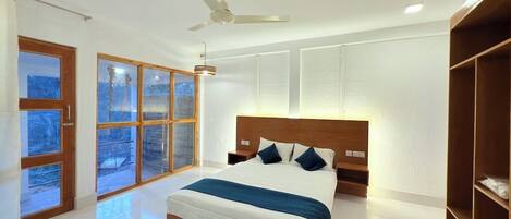 A modern bedroom with a large bed, a ceiling fan, and a view through the windows.
