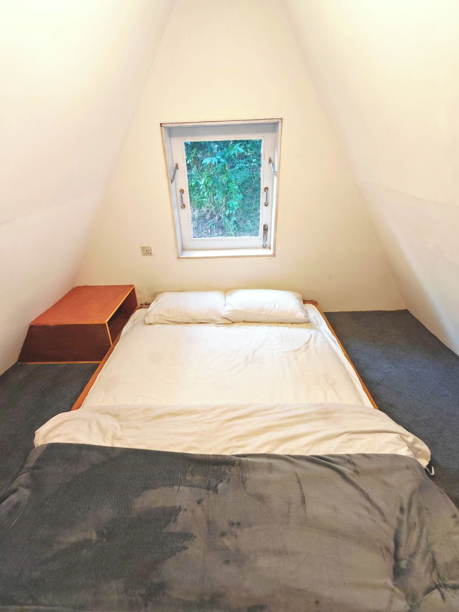 Ein kleiner, dreieckiger Raum mit einem Bett, einem Fenster und einer hölzernen Bank.