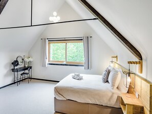 A bedroom with a sloped ceiling, a bed with pillows, a desk with a chair, a window, and a hanging light fixture.