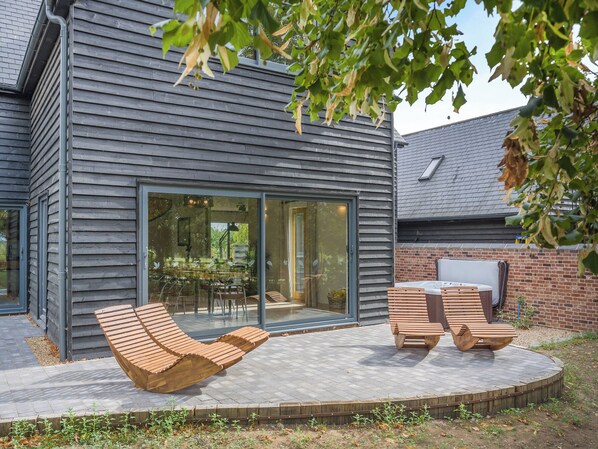 A modern house with a patio, two wooden lounge chairs, and a glass door leading to an interior space.