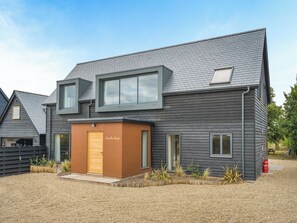 A modern two-story house with a sloped roof, a small attached garage, and a gravel driveway.