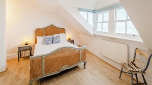 Ein Schlafzimmer mit einem Rattanbett, einem Holzstuhl, einem Nachttisch, einem Fenster und einem Oberlicht.