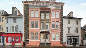 Ein mehrstöckiges Gebäude mit rosa Fassade, steinernen Basis und einem Hauseingang an der Ecke.