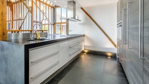A modern kitchen with a wooden beam ceiling, stainless steel appliances, and a large window.