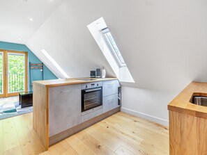 Une cuisine moderne dotée d’une verrière, d’un plancher en bois et offrant une vue sur la verdure environnante.