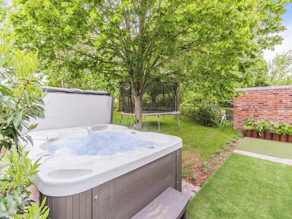 Un jacuzzi dans un jardin, avec un trampoline, un mur en briques et un arbre.