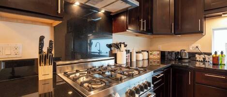 A modern kitchen with dark wooden cabinets, stainless steel appliances, and a black countertop.