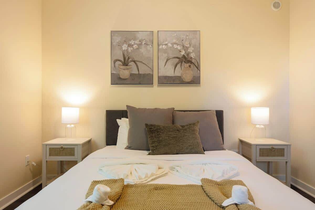 Ein Hotelzimmer mit einem großen Bett, zwei Nachttischen mit Lampen und zwei an der Wand befestigten Blumenbildern.